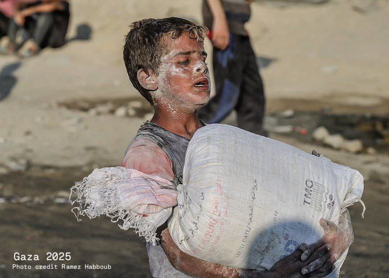 A hungry child is struggling to carry a heavy flour bag obtained from aid truck northwest of Gaza Ci